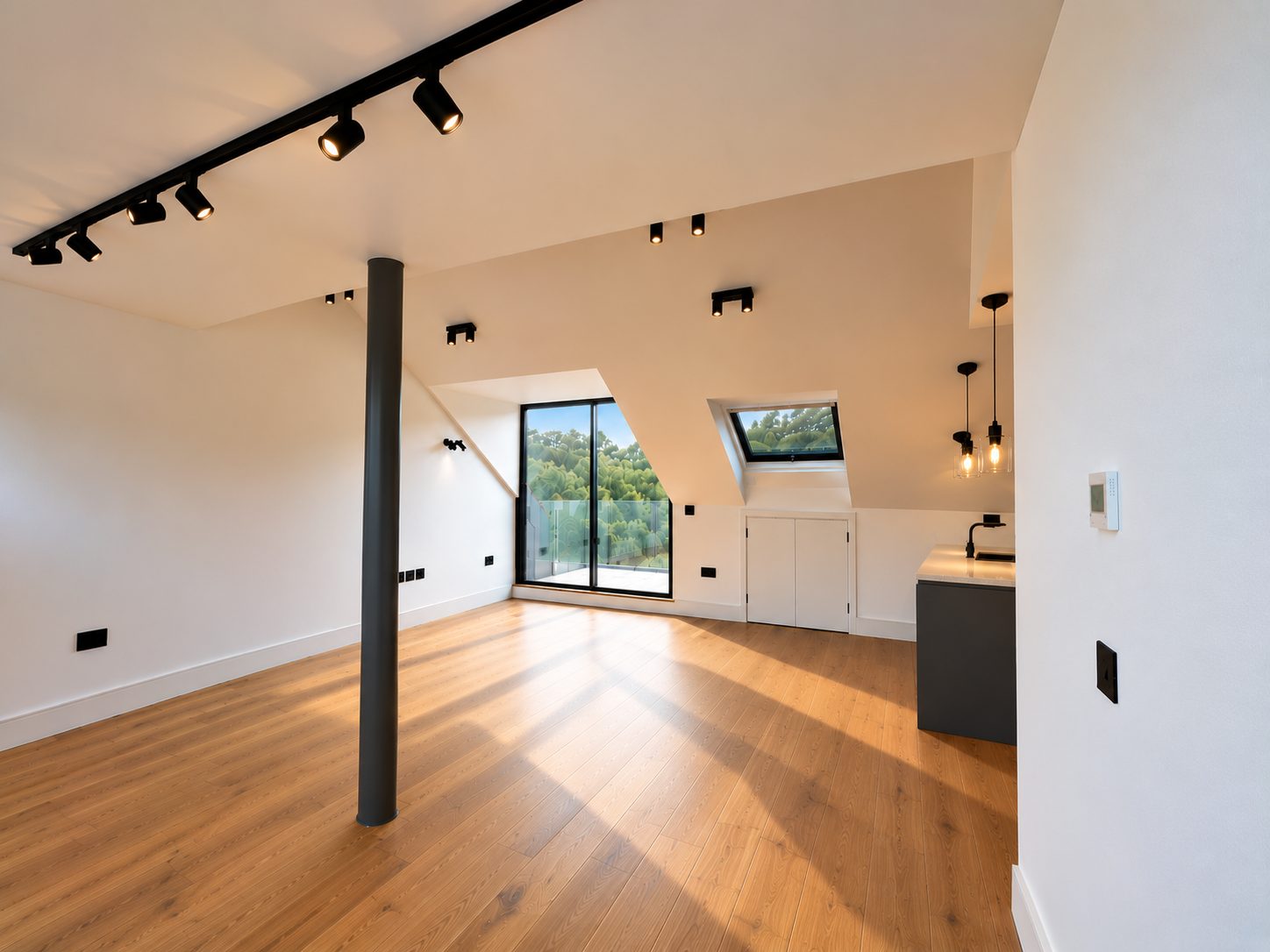 Unit 12 open-plan living space: wood floors, track lighting and a dark column, with glazed doors to a balcony and the kitchen to one side.